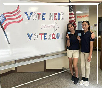 Two students in front of a vote here sign
